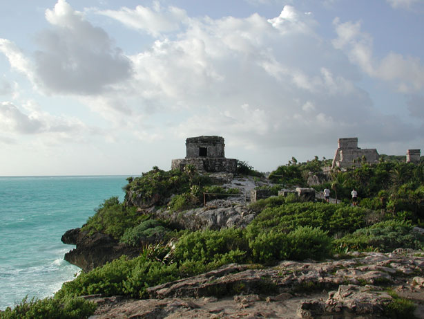 Mayan ruins sit on a bluff of rock covered with low scrub overlooking the Caribbean. Below, waves crash against the rocks.