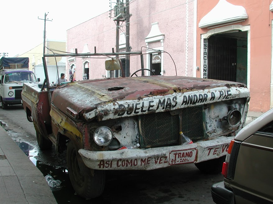The rusted carcass of a truck parked on the side of the street. Painted across the front: Duele mas andar a pie (it hurts more to walk). On the bent and twisted remains of the bumper: Asi como me vez te veras (one day, you'll look like this too).
